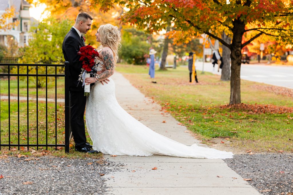 Newlyweds share a quiet moment with a red rose bouquet on an autumn street in Brandon, Vermont.