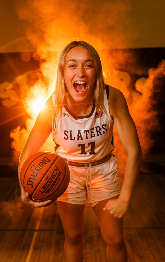 High school basketball player holding a ball in a uniform with dramatic orange lighting