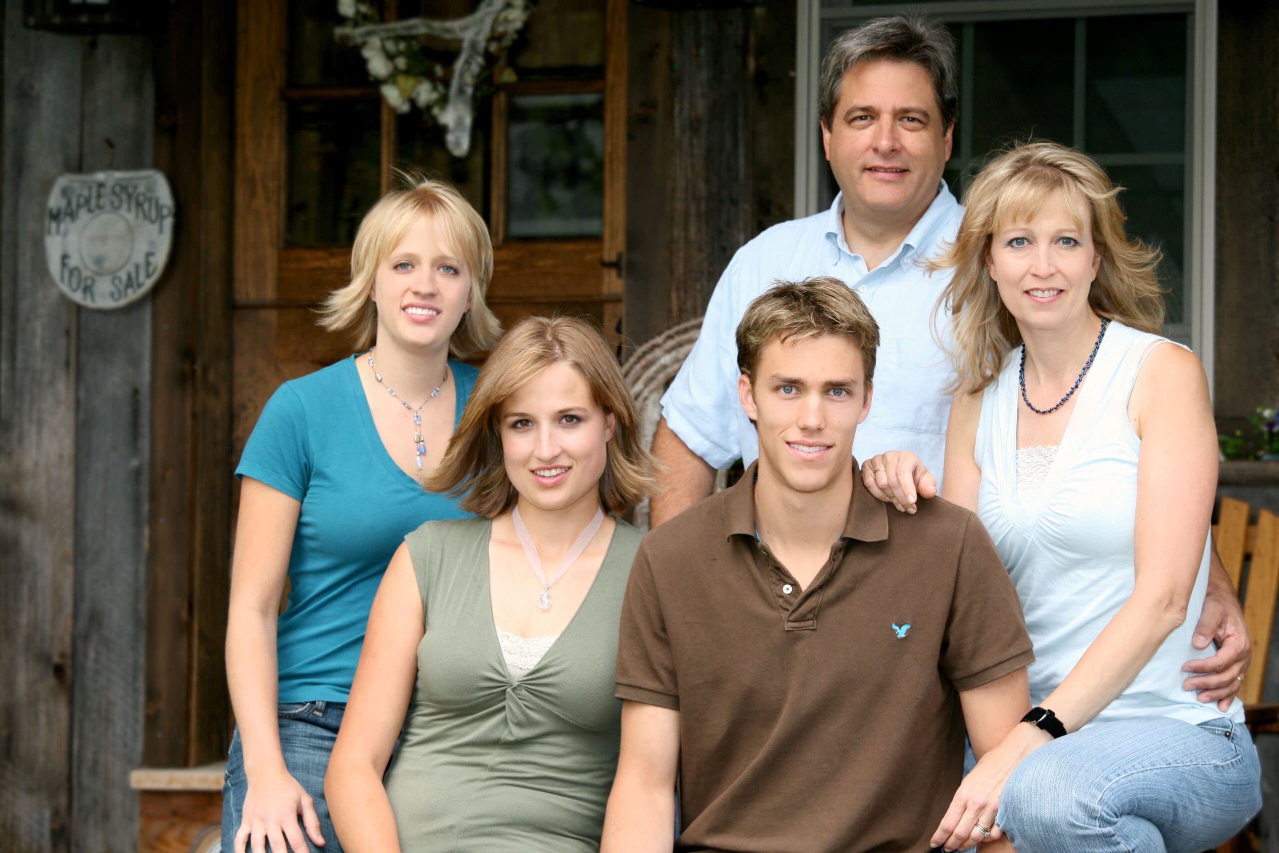 A family of five poses together outside a rustic maple sugarhouse.