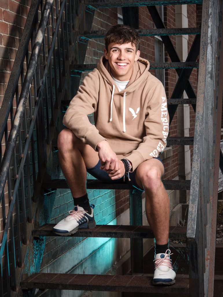 High school senior sitting on a metal staircase in a casual hoodie and sneakers