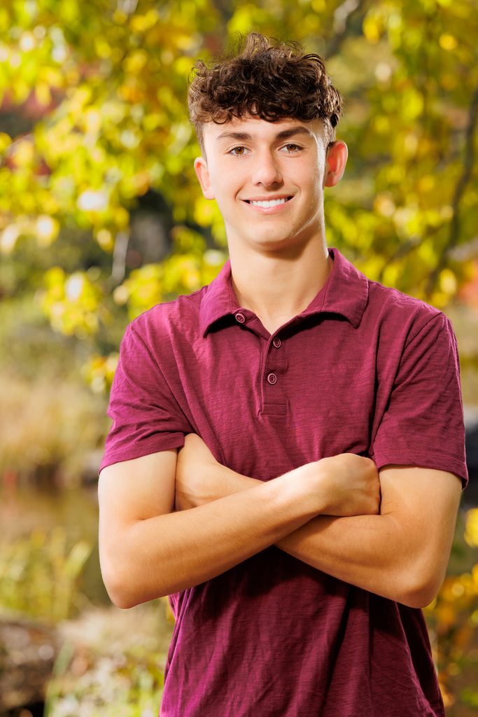 High school senior standing outdoors in a maroon shirt with autumn leaves in the background