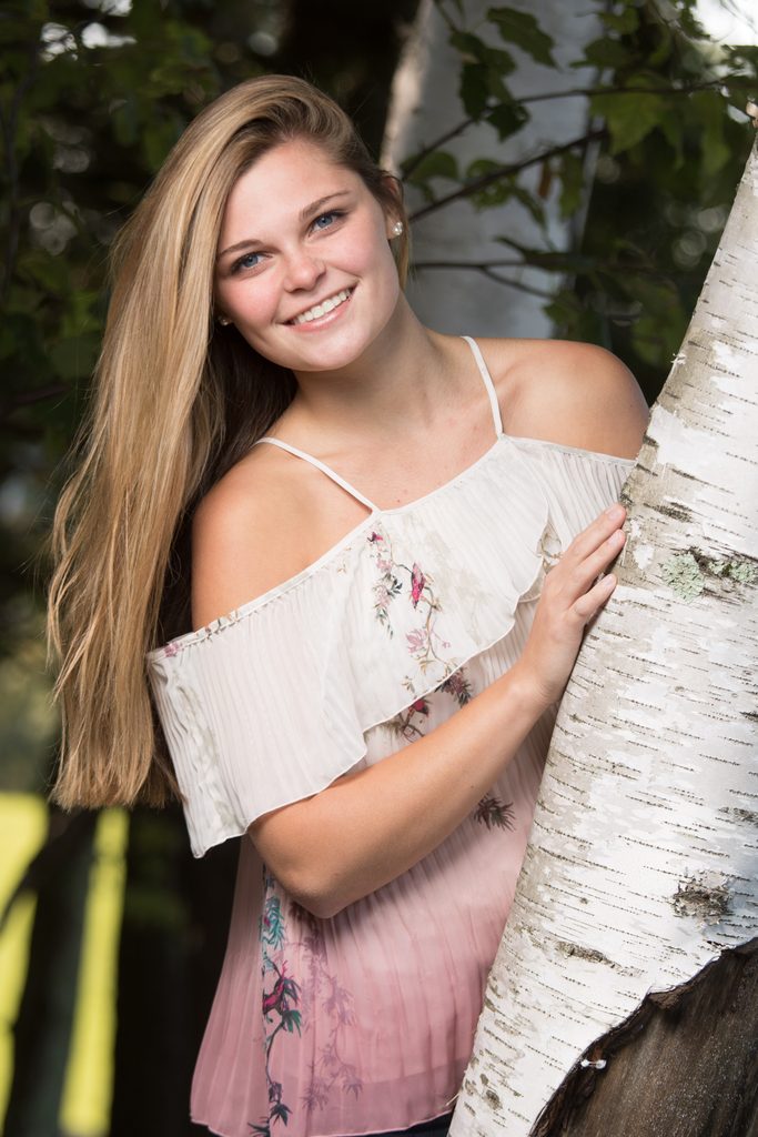 High school senior smiling beside a birch tree in a floral outfit