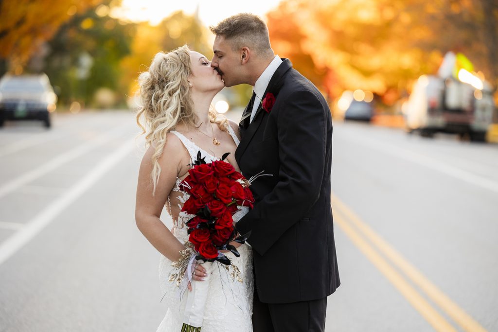 Couple kissing  in the middle of the street after their wedding at The Lilac Inn in Brandon Vermont, with Vermont fall foliage behind them. 
